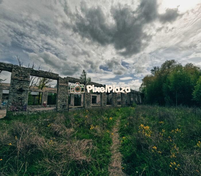 Abandoned Stone Building Ruins Under Dramatic Sky in Overgrown Field