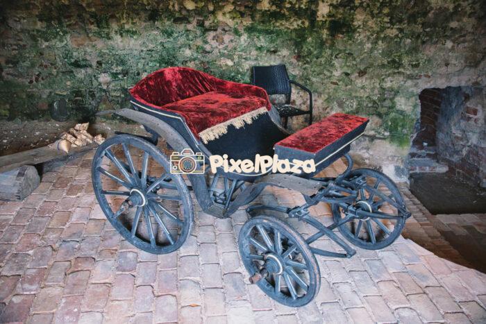 Antique Horse-Drawn Carriage with Red Velvet Upholstery in Rustic Setting
