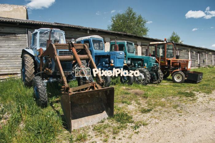 Old Soviet Tractors Parked in Front of Rural Garages on a Sunny Day Old Soviet Tractors Parked in Front of Rural Garages on a Sunny Day