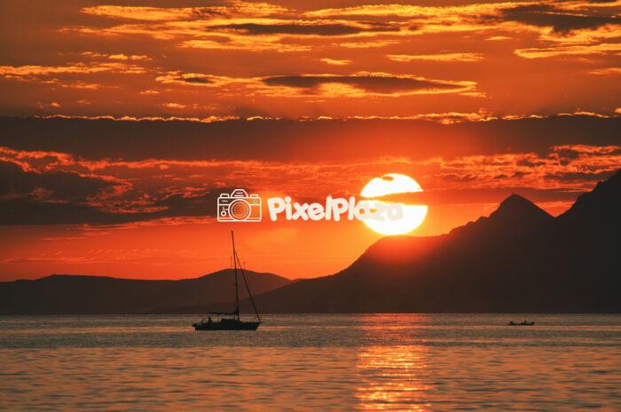 Golden Sunset Over Adriatic Sea with Silhouetted Sailboat and Mountains