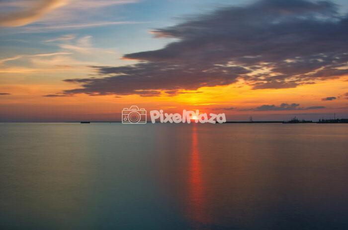 Dramatic Sunset Over Calm Sea with Silhouetted Harbor - Peaceful Evening Sky