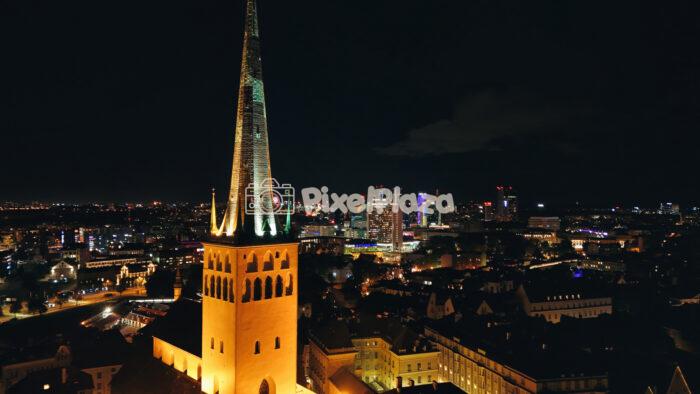 Illuminated St. Olav's Church Spire and Tallinn's Contrasting Skyline at Night