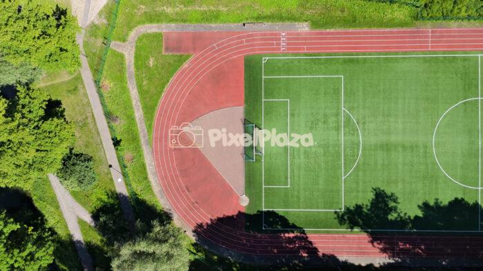 Top down drone shot of green football field and red running track stadium