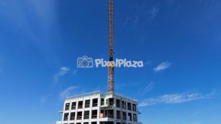 Yellow tower crane on modern building under construction with blue sky